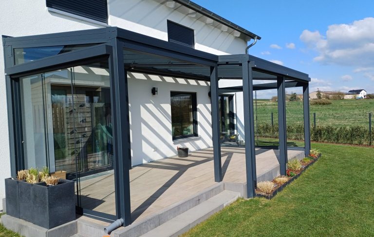 Überdachte Terrasse Überdachte Terrasse mit Glaswänden an einem modernen Gebäude, umgeben von Rasen.